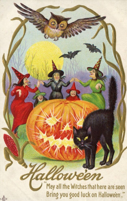 A vintage postcard of witches wearing pointy hats and dancing around a giant jack o'lantern. An owl and bats appear in the sky above a full moon, and a black cat hisses near the jack o'lantern.